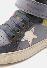 Zapatillas altas de cuero gris con un acento de estrella, cordones azules y una correa de gancho y bucle. Incluyen detalles perforados y una suela texturizada.