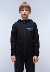 Zwarte rits hoodie gemaakt van zachte stof, met een capuchon, een logo op de linkerborst, kangoeroezakken en ribgebreide manchetten. Gecombineerd met zwarte broek.
