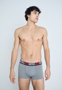 Boxer-briefs gris avec une ceinture en logo Diesel noire et rouge. Matériau en coton, design ajusté, texture douce. Le modèle pose de côté.