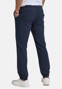 Marineblaue Jogginghosen mit elastischem Bund, Seitentaschen und gerippten Bündchen. Der Stoff hat eine glatte Textur und verfügt über eine hintere Knopftasche.