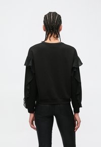 Zwarte sweatshirt met geplooide, doorschijnende stofaccenten op de mouwen, een ronde halslijn en een aansluitende zoom, gecombineerd met glanzende zwarte broek.