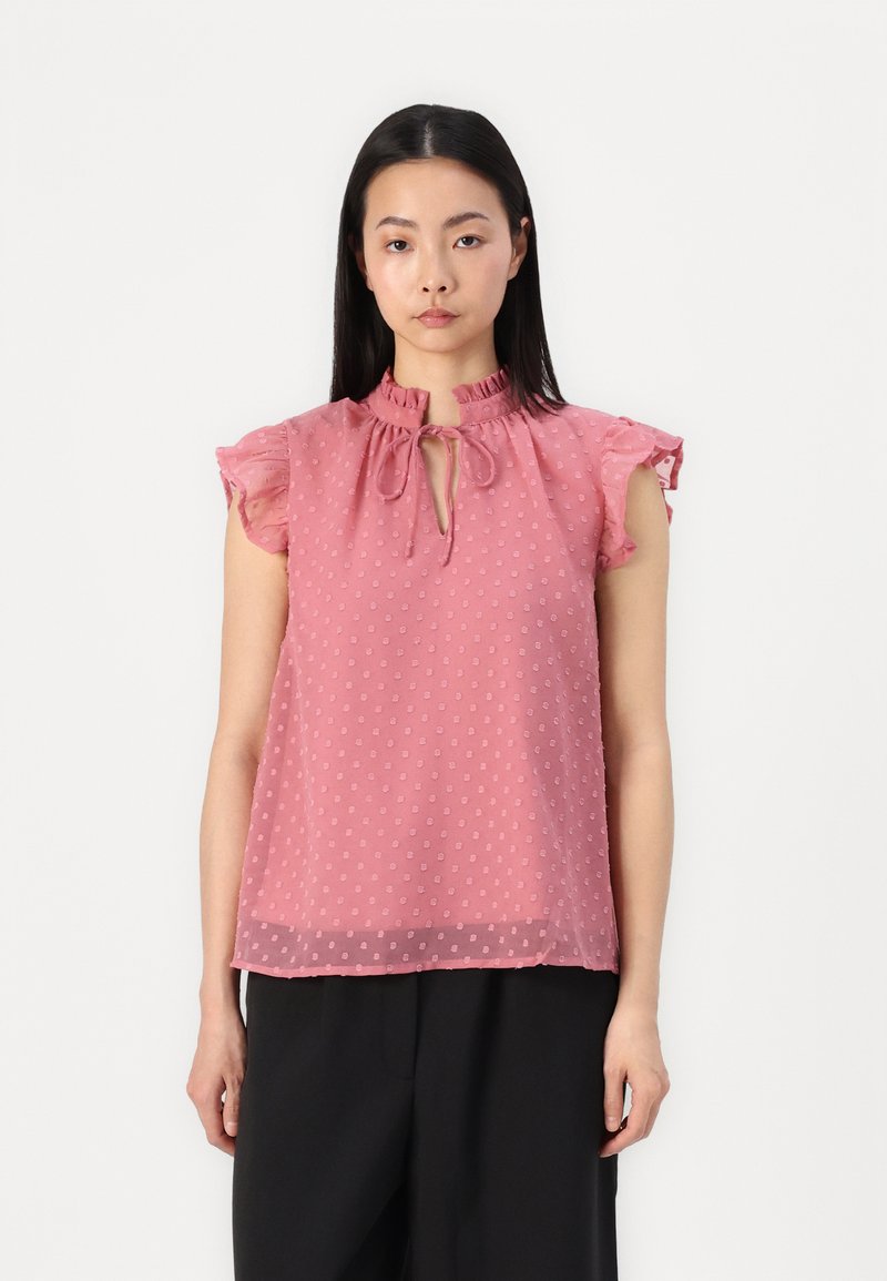 Top in chiffon rosa con motivo a pois, maniche corte arricciate, scollatura a occhiello con dettaglio di lacci e una silhouette ampia.