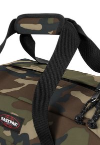 Borsa da viaggio con motivo camouflage, manici in rete nera, tracolla superiore e chiusura con zip. Presenta un'etichetta con il logo Eastpak.