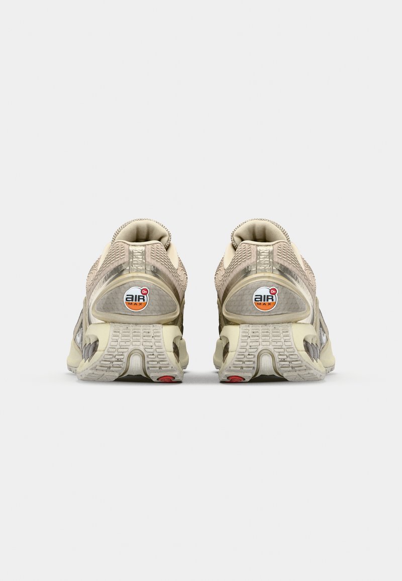 Beige und graue Sneakers mit einem Mesh-Obermaterial, sichtbarer Luftpolsterung, strukturiertem Absatz und Gummi-Außensohle mit roten Akzenten.