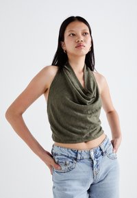 Olive roheline, varrukateta, drapeeritud ülemine osa koos kaitsva kaelusega, kokku sobitatud kõrge vöökohaga helesiniste denimriidest teksadega, millel on pleekinud tekstuur.