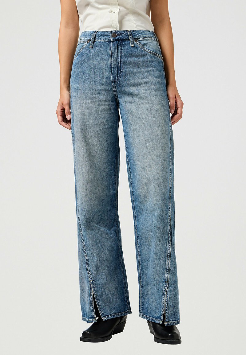 Ljusblå vida jeans i denim, med framfickor, synlig sömnad och sprund i fållen. Bärs med svarta stövlar.