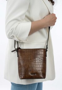 Borsa a tracolla in pelle marrone con stampa a coccodrillo, con una corta tracolla nera, forma rettangolare e superficie liscia. Inclusi dettagli in metallo.
