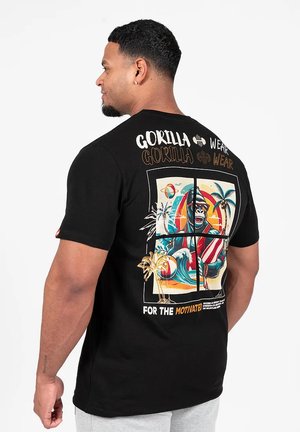Zwarte katoenen t-shirt met kleurrijk grafisch ontwerp op de achterkant, inclusief een gorilla, palmbomen en de tekst "VOOR DE GEMOTIVEERDEN."