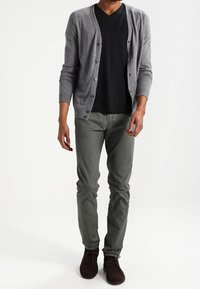 Grå cardigan över en svart V-ringad t-shirt, kombinerat med gröna byxor och mörkbruna skor. Har knappar på cardiganen och en slim fit.