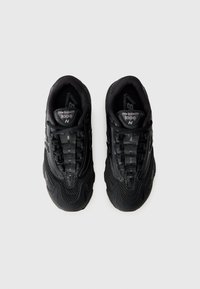Sorte sneakers med mesh-overdel, polstret krave, cushioned sål og fremtrædende "N" logo på tungen. Struktureret design med reflekterende accenter.