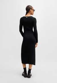 Black ribbed long-sleeve dress with a fitted silhouette, side slits, and a raw hem. The model wears chunky black platform shoes and ankle socks.