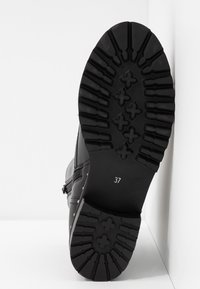 Botte noire avec une semelle en caoutchouc texturé présentant un motif de semelle. La taille indiquée comme 37 est visible sur le talon.