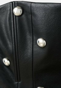 Čierna koženka s textúrovaným povrchom, zdobená výraznými striebornými cvokmi a vertikálnym prešívaním.