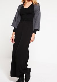 Černé široké kalhoty spojené s přiléhavým černým topem a šedým kimono-style sáčkem s volnými rukávy. Hladká látka se volným střihem.