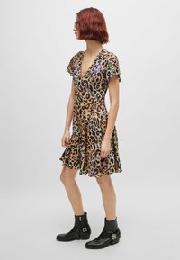 Leopard print dress in lightweight fabric, features a deep V-neck, short flutter sleeves, and a flared, ruffled hem. Paired with black ankle boots.