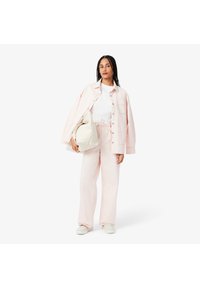 Chemise rose surdimensionnée, t-shirt blanc et pantalon rose assorti. Le modèle tient un sac crème. La tenue présente une coupe décontractée et un tissu doux.
