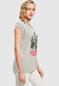 Hallidehalli lühikeste varrukate ja graafikaprindiga t-särk, kus on kujutatud tegelasi jalgratastel, all on roosa tekst "Stranger Things".