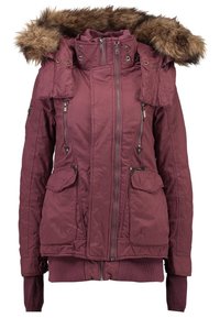 Veste d'hiver bordeaux avec capuche bordée de fourrure, fermeture éclair frontale, deux poches poitrine zippées et deux poches à rabat à la taille.