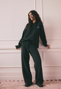 Dunkelgrauer übergroßer Hoodie und locker sitzende Hose, beide aus einem weichen Material, mit bestickten Akzenten einer Hand und dem Text "Lucky Star."