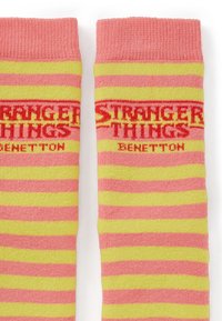 Calzini al ginocchio con strisce orizzontali rosa e gialle. "STRANGER THINGS" e "BENETTON" sono ricamati in rosso nella parte superiore.