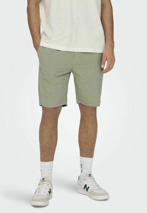 Pantalones cortos verdes de tejido texturizado, corte recto y bolsillos laterales, combinados con zapatillas blancas y calcetines deportivos blancos.