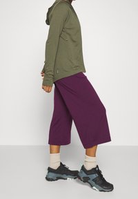 Olivgrön zip-up hoodie med långa ärmar, i kombination med lila culotter. Svarta sportskor med grå detaljer och ljusa strumpor.