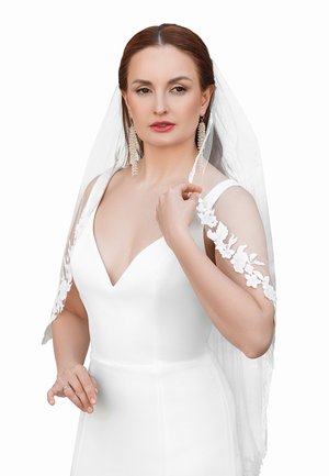 White wedding dress with a plunging neckline and floral lace sleeves. Sheer veil, statement earrings, and a subtle ring on her finger.