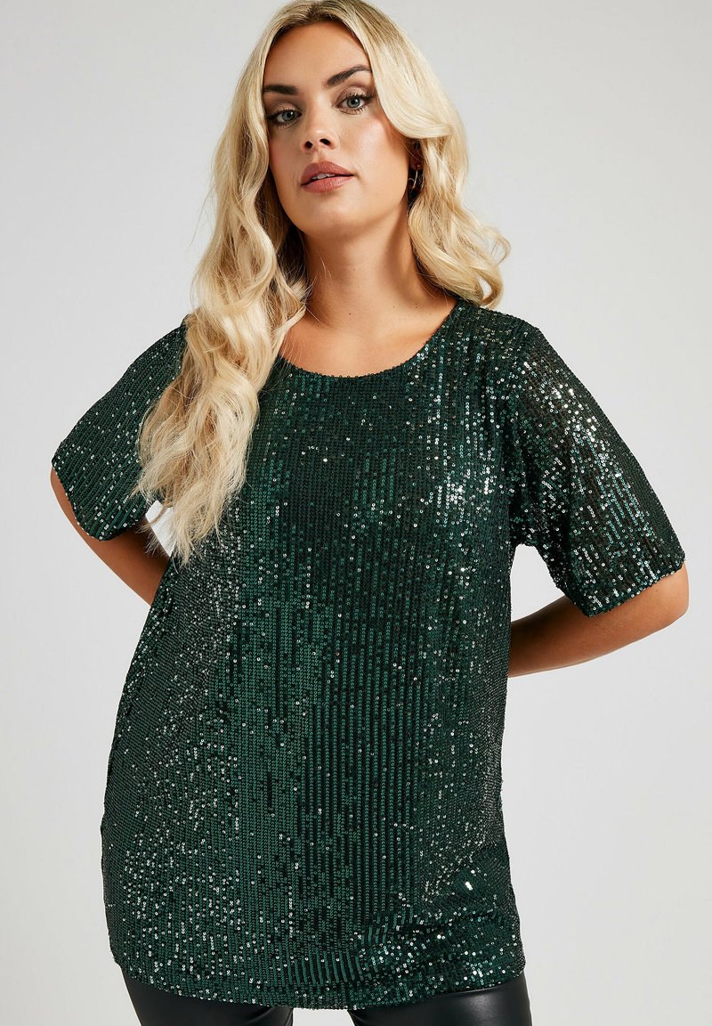 Top verde con paillettes, maniche corte, scollatura rotonda e vestibilità ampia. Texture scintillante con motivo a righe verticali.