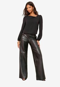 Bluză neagră cu mâneci lungi, cu decolteu drapat și un accent decorativ. Asortată cu pantaloni largi, cu talie înaltă, din piele ecologică neagră.