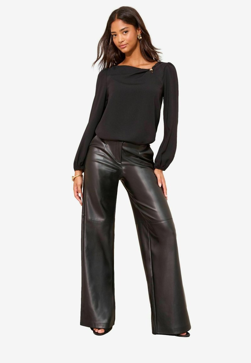 Bluză neagră cu mâneci lungi, cu decolteu drapat și un accent decorativ. Asortată cu pantaloni largi, cu talie înaltă, din piele ecologică neagră.