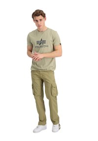 Olivengrøn t-shirt med grafisk logo og cargo-bukser i matchende olivengrøn, med cargo-lommer, stylet med hvide sneakers.