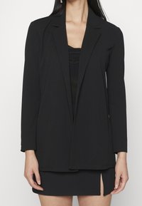 Czarny długi żakiet z kołnierzem szalowym i otwartym przodem, wykonany z lekkiego materiału, z długimi rękawami i luźnym krojem.