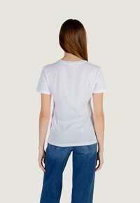 White cotton t-shirt with a round neckline and short sleeves. Features a relaxed fit and a plain design, paired with blue wide-leg jeans.