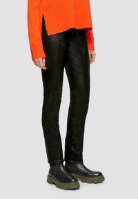 Schwarze Kunstlederhose kombiniert mit einem leuchtend orangefarbenen Pullover. Die Hose hat eine schmale Passform, und der Pullover hat gerippte Bündchen und einen gerippten Saum.