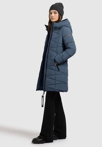 Námornícky modrá puffer bunda s prešívaným dizajnom, kapucňou a bočnými vreckami, skombinovaná s čiernymi rozšírenými nohavicami a platformovými čižmami.