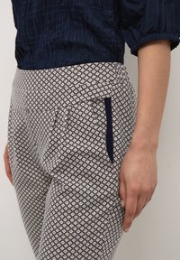 Byxor i marinblått och krämfärgat mönster har en geometrisk design, sidofickor med marinblå detaljer och en jämn textur.