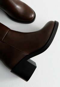 Stivaletti in pelle marrone con un design elegante, punta arrotondata e tacco a blocco. Presentano una superficie liscia e dettagli di cucitura lungo i lati.