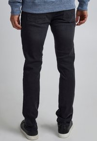 Jeans de mezclilla negra con un corte ajustado, con costuras sutiles en los bolsillos traseros y una textura desgastada. Combinados con zapatillas bajas negras.