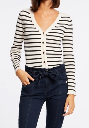 Cardigan côtelé à rayures en crème et noir, avec un col en V, une fermeture à boutons et une coupe ajustée, associé à un pantalon taille haute bleu marine.