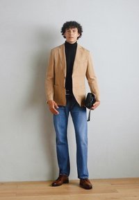Beige op maat gemaakte blazer, zwarte turtleneck, blauwe jeans, bruine leren schoenen, met een kleine zwarte tas. Gladde texturen en een aansluitend ontwerp.