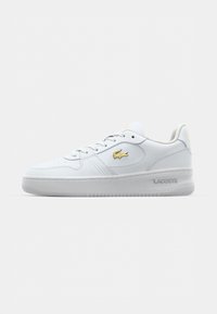 Baltos odinės sportbačiai su lygiu paviršiumi, apvaliu galiuku ir raištelių užsiejimu. Šone ir ant kulno yra auksinė Lacoste logo. Guminis padas.