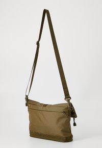 Borsa a tracolla khaki realizzata in nylon testurizzato con tracolla regolabile, chiusura superiore a zip e tasca frontale. Presenta una forma rettangolare elegante.