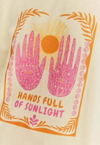 Krémové tričko s grafickým motivem dvou rukou v růžové barvě s jemnými vzory, obklopené oranžovými akcenty a slunečním motivem.