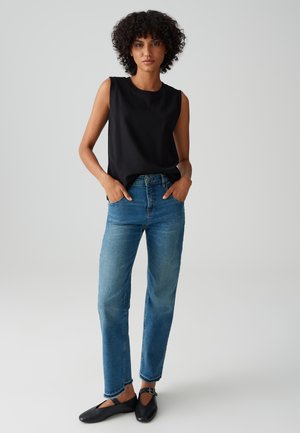 Top noir sans manches, jeans droits bleus et chaussures plates noires. Tissu doux, design simple et légers effets de déchirure aux ourlets des jeans.