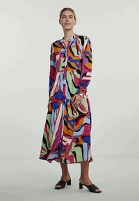Colorful long dress featuring a mix of abstract patterns in purple, green, orange, and blue; button-down front; long sleeves; lightweight fabric.