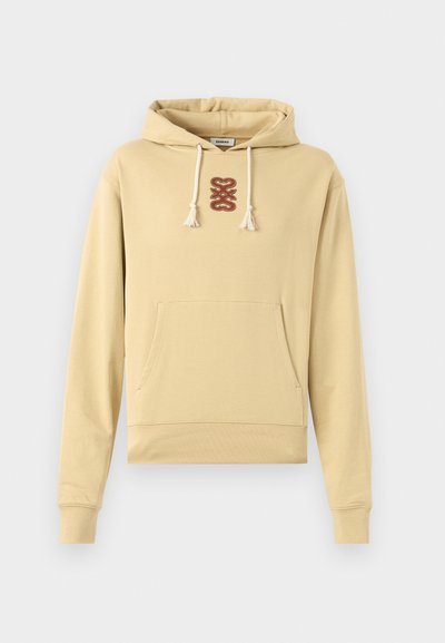 Beige hettegenser med frontlomme, hvite snorer og et sentralt brunt abstrakt broderi under hetteåpningen.