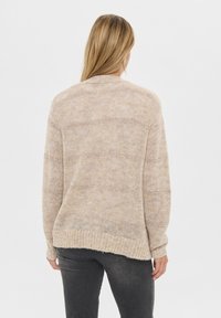 Beżowy sweter dzianinowy o luźnym kroju, z teksturowanym wzorem, ściągaczami na mankietach i dolnym końcu. Widok z tyłu pokazuje projekt w stylu high-low.