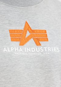 Szara bluza z kapturem z wyrazistym pomarańczowym logo o trójkątnym kształcie oraz napisem "ALPHA INDUSTRIES" i lokalizacją w białym kolorze.
