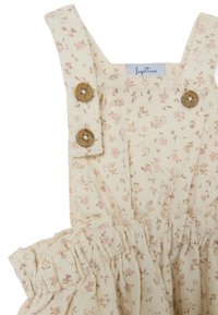 Bloemmotief, crèmekleurige jurk met verstelbare bandjes, houten knopen en een geraffineerde taille. Heeft een zachte, gestructureerde stof met roze accenten.
