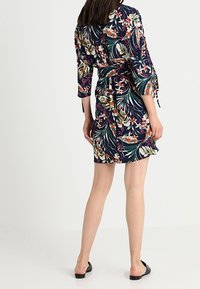 Vestido envolvente floral en azul oscuro, con vibrantes patrones tropicales, mangas tres cuartos, cinturilla ajustada y falda hasta la rodilla.